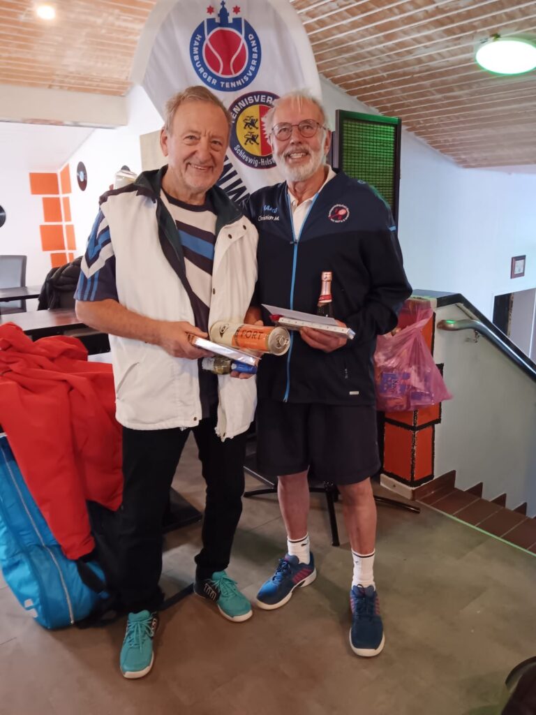 Der neue Landesmeister Ulli Rubehn (links) und Finalist Christian Monecke (rechts) stehen lächelnd nebeneinander im Clubhaus. Rubehn hält eine Dose Tennisbälle und einen Preis, Monecke eine kleine Flasche Sekt. Im Hintergrund ist das Banner des Tennisverbands zu sehen.